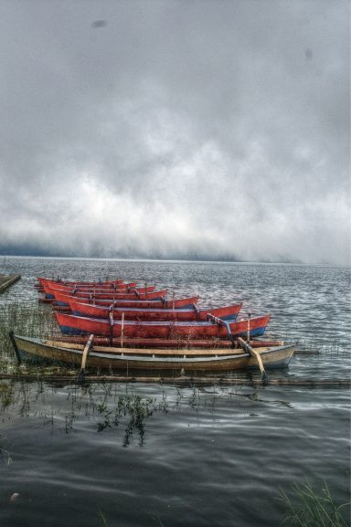 Rode boten liggen aan de oever van een meer onder een bewolkte lucht.